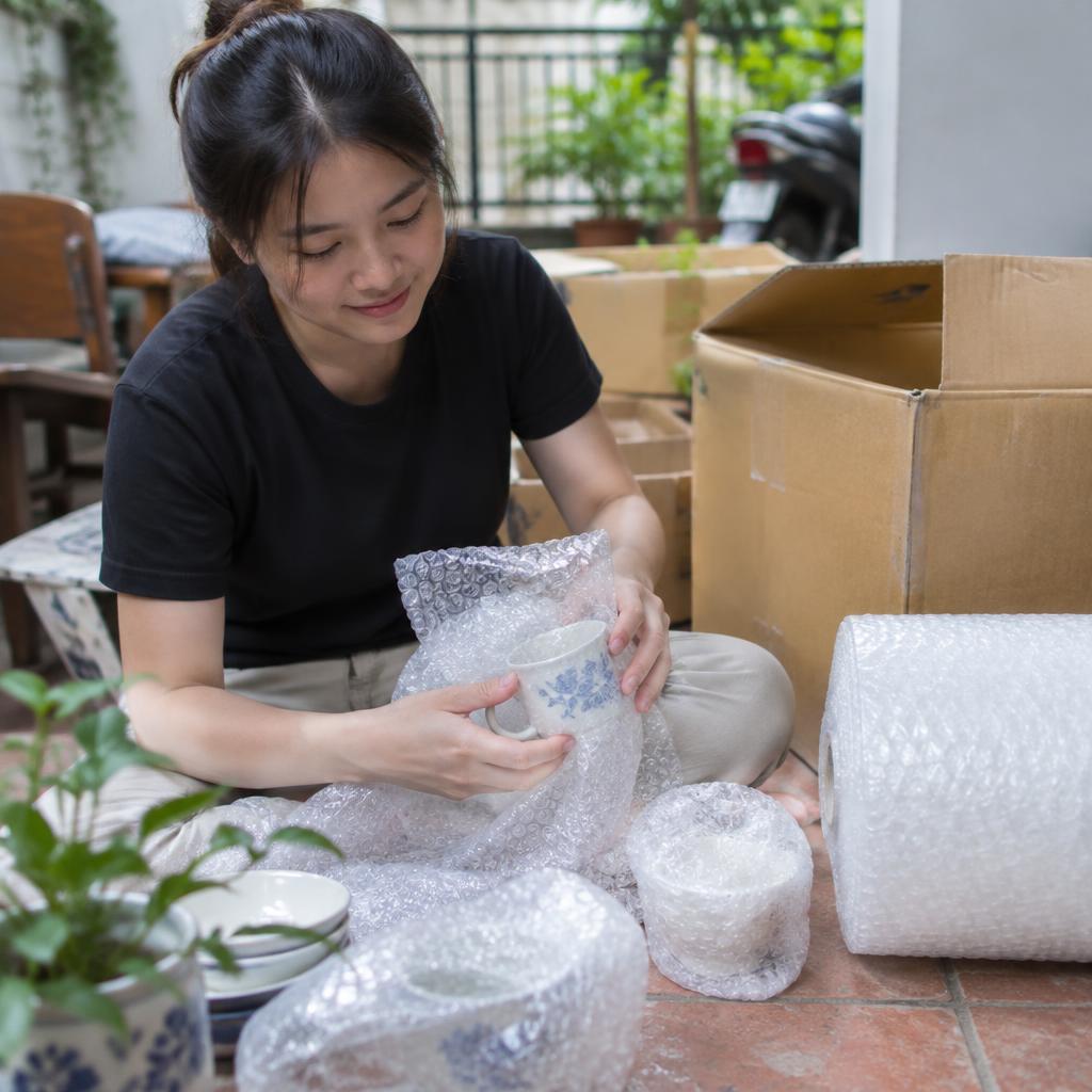 Hộp carton ghi chữ 'FRAGILE' (Dễ vỡ) và 'HANDLE WITH CARE' (Cẩn thận) đang được đóng gói với vật liệu bảo vệ.
